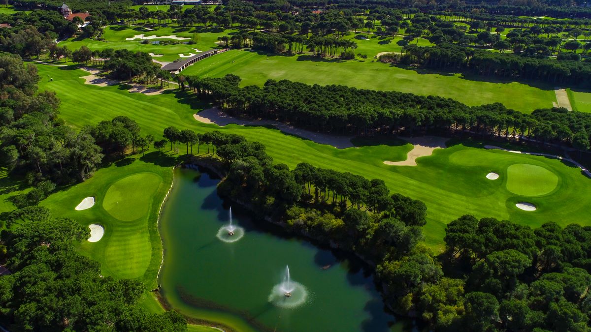 Montgomerie Maxx Royal Golf Course from the air, showing a lake, water features, green trees and multiple fairways