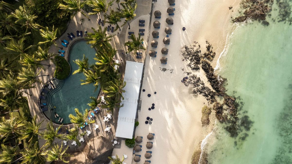 Beach and sun loungers in front of palm trees at Constance Belle Mare Plage Hotel Mauritius