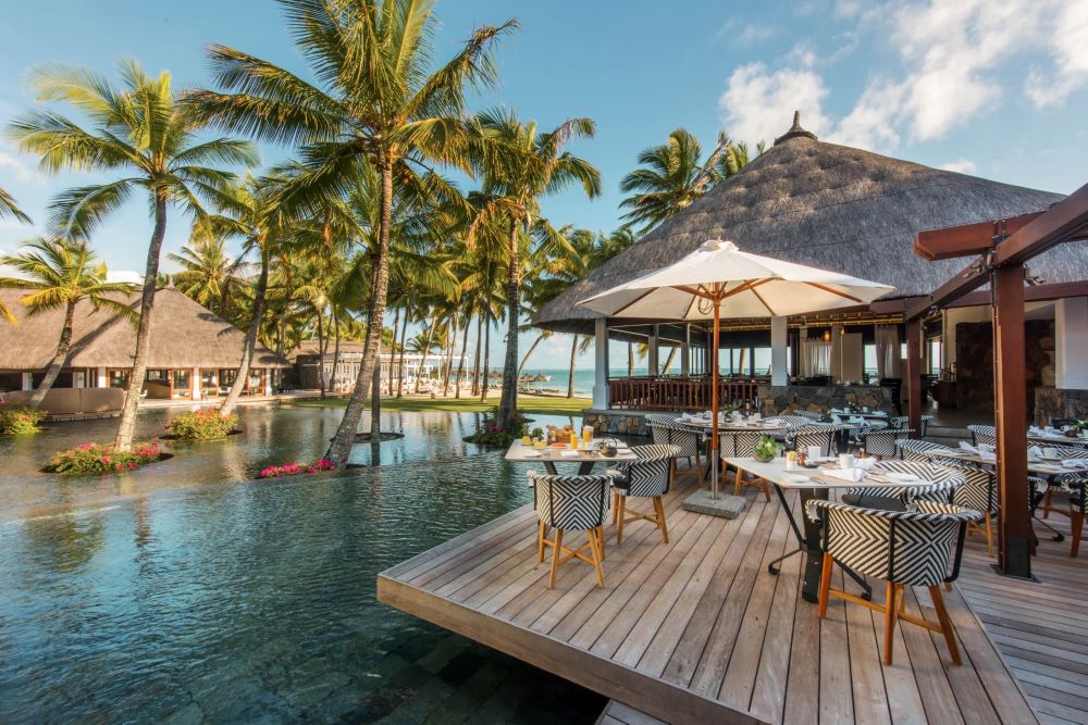 Palm trees by pool overlooked by dining table at Constance Belle Mare Plage Hotel Mauritius