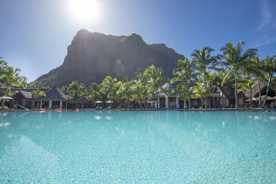 Sun shining over the mountain with swimming pool in foreground at Dinarobin Beachcomber Golf Resort & Spa