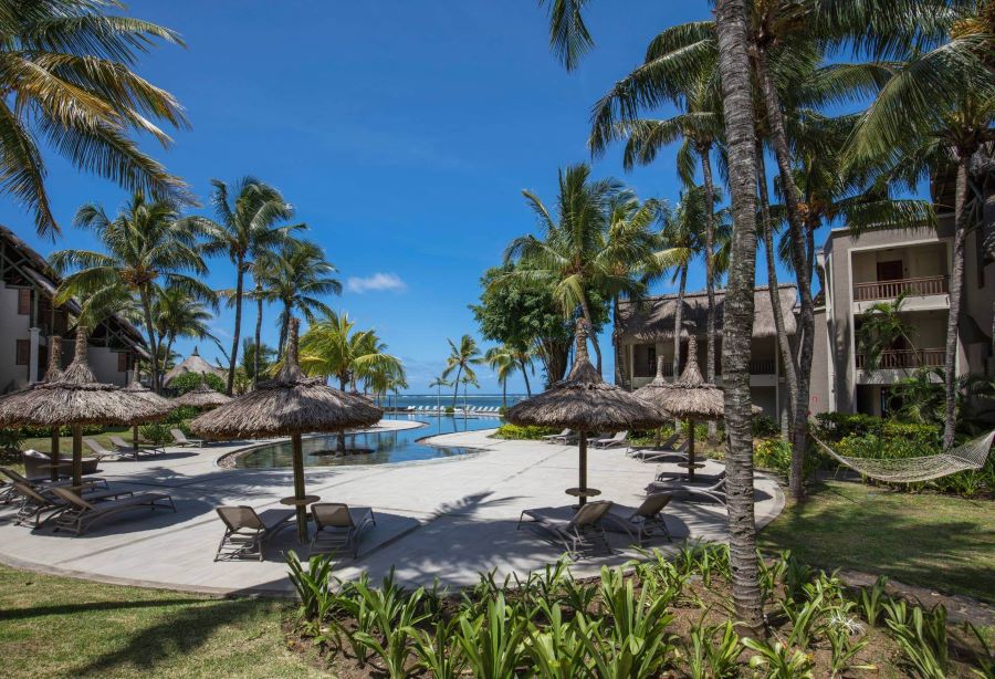 Beach with sun loungers under palm trees and blue sky at Heritage Awali Golf & Spa Resort