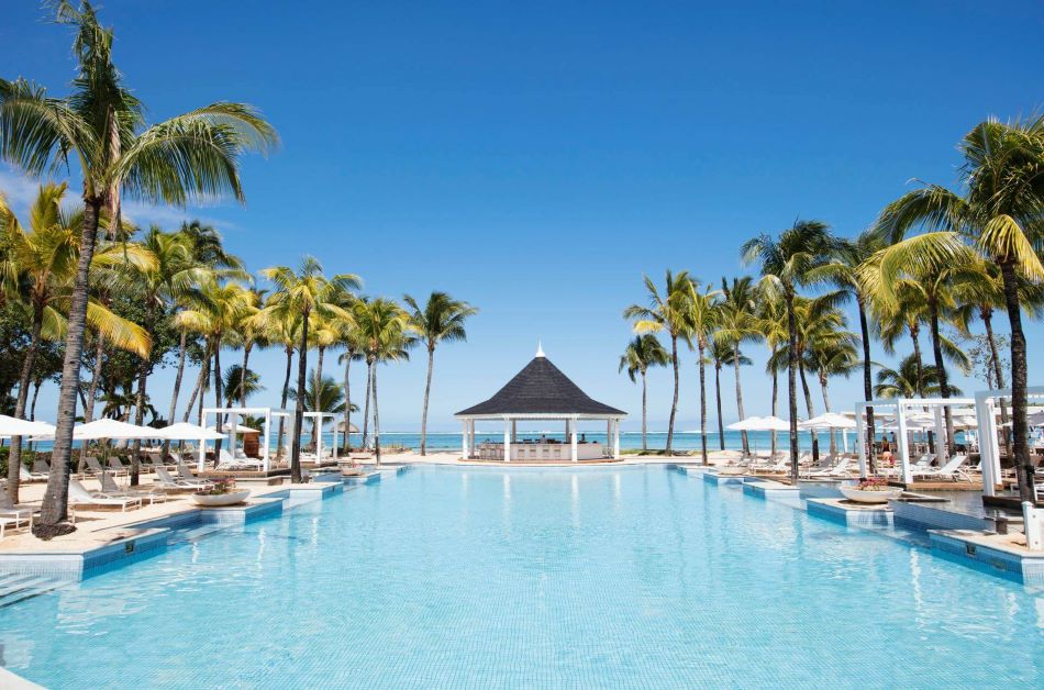 View of the swimming pool and pool bar, lined with palm trees at Heritage Le Telfair Golf & Wellness Resort in Mauritius