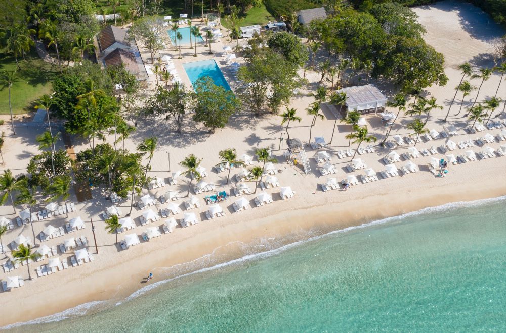 Beach with sun loungers and parasols and swimming pool behind at Casa de Campo Resort & Villas