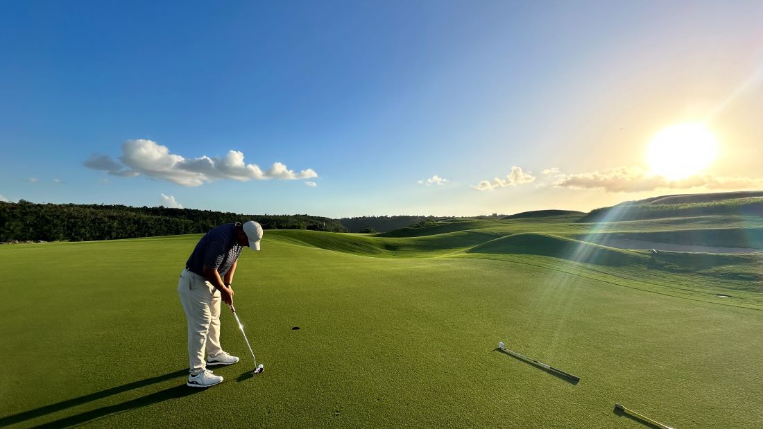 Golfer on putting green with blue sky and sunshine overhead at Dye Fore