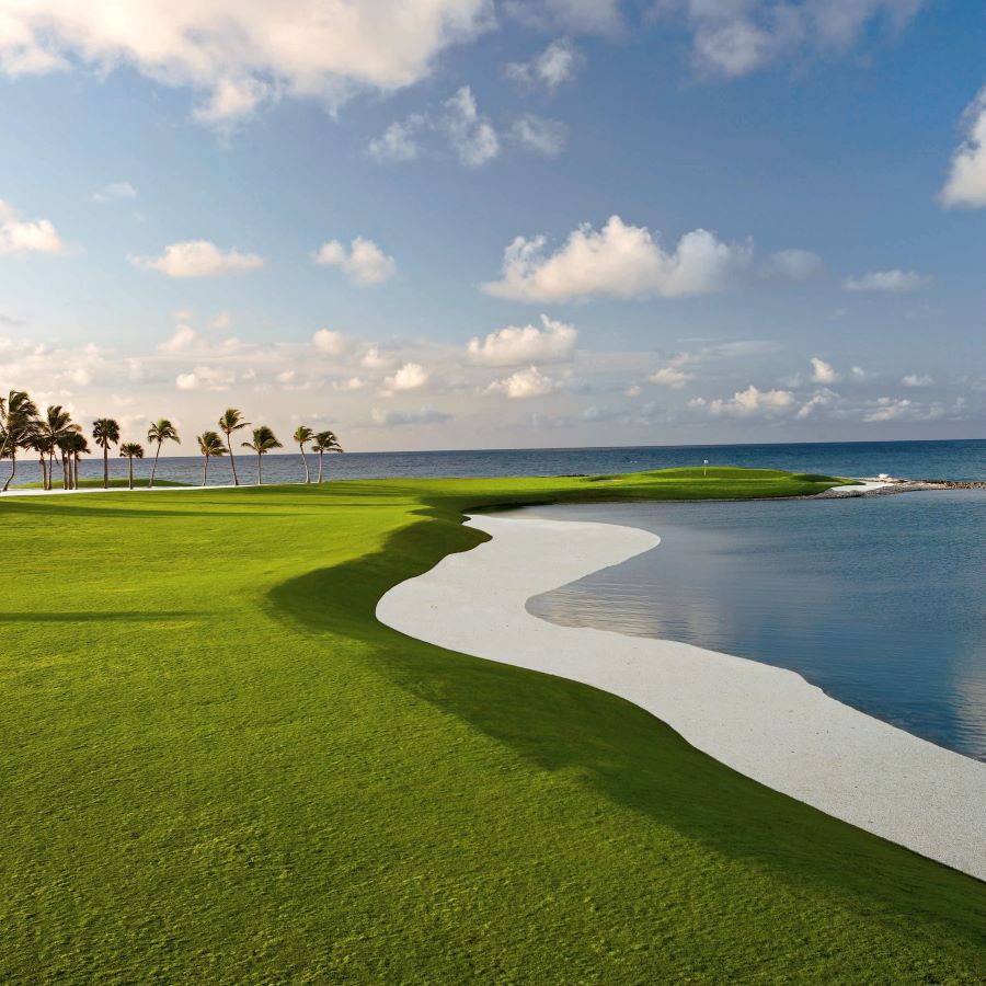 Blue sky with white clouds over the fairway with water and sand dune to the right of the golf course at Punta Espada Golf Club