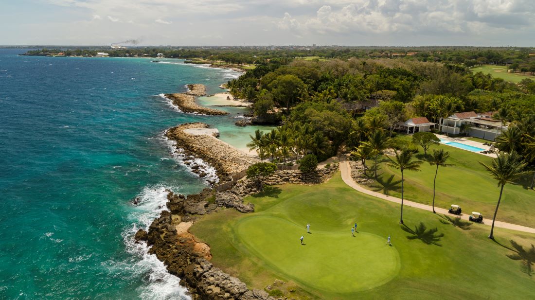 Putting green surrounded by the sea, rocks, and trees at Teeth of the Dog Golf Course