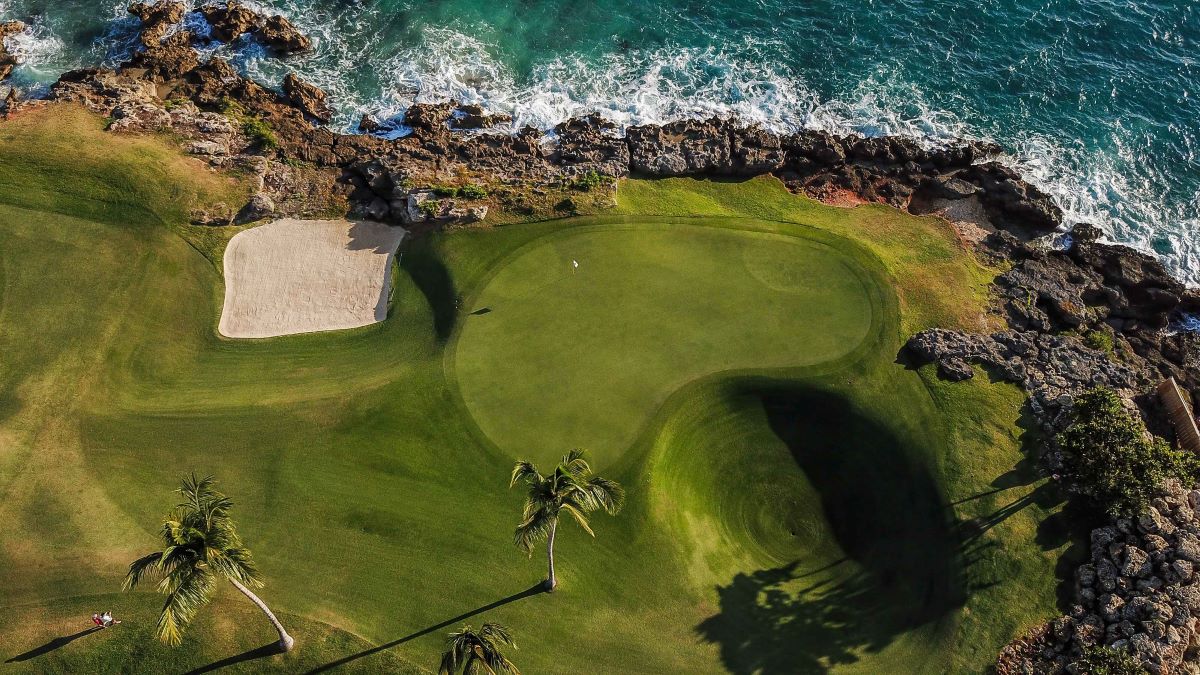 Drone shot of the putting green on the golf course at Teeth of the Dog with waves lapping against the rock protecting it