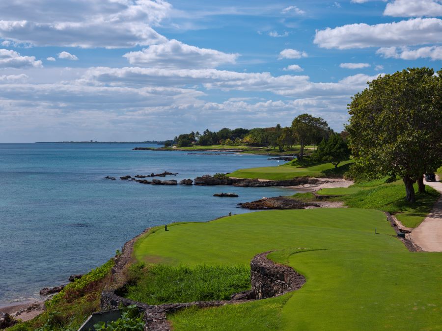 Blue sea and sky with white clouds overlooking the green grass fairway at Teeth of the Dog in Dominican Republic