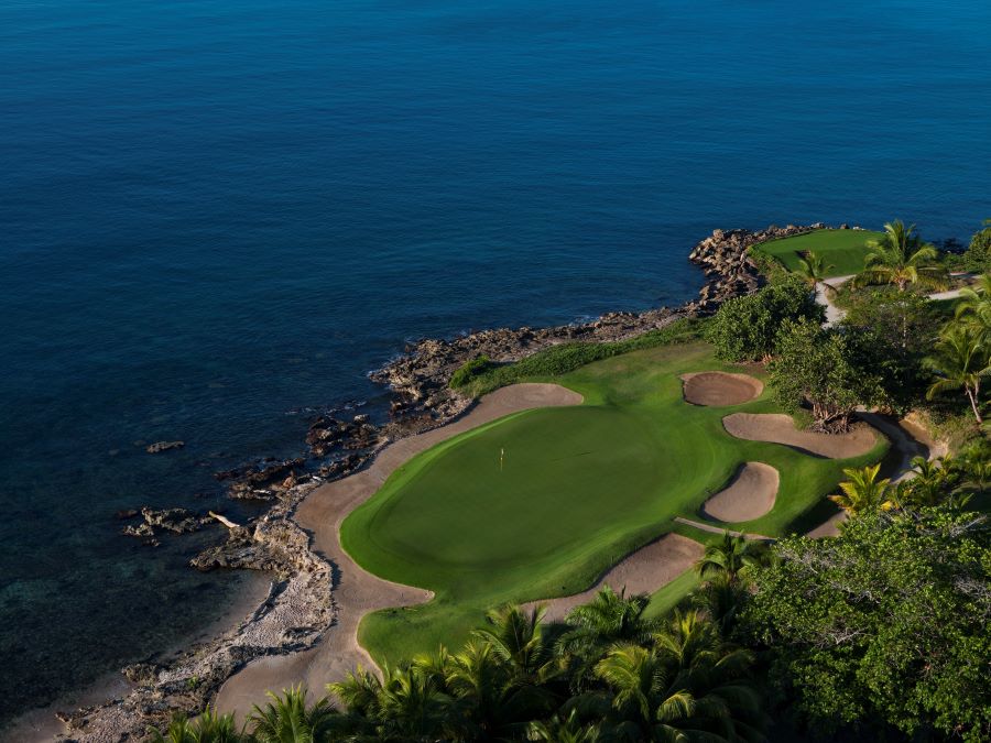 Deep blue sea surrounding one side of Teeth of the Dog golf course, and sand bunkers protecting the green on the other