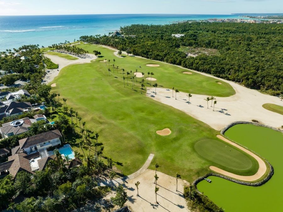 Green trees to the right of the golf course and blue ocean in front of it at La Cana Golf