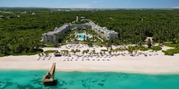 View of The Westin Puntacana Resort & Club with white sand beach and turquoise water in front of it and green trees behind