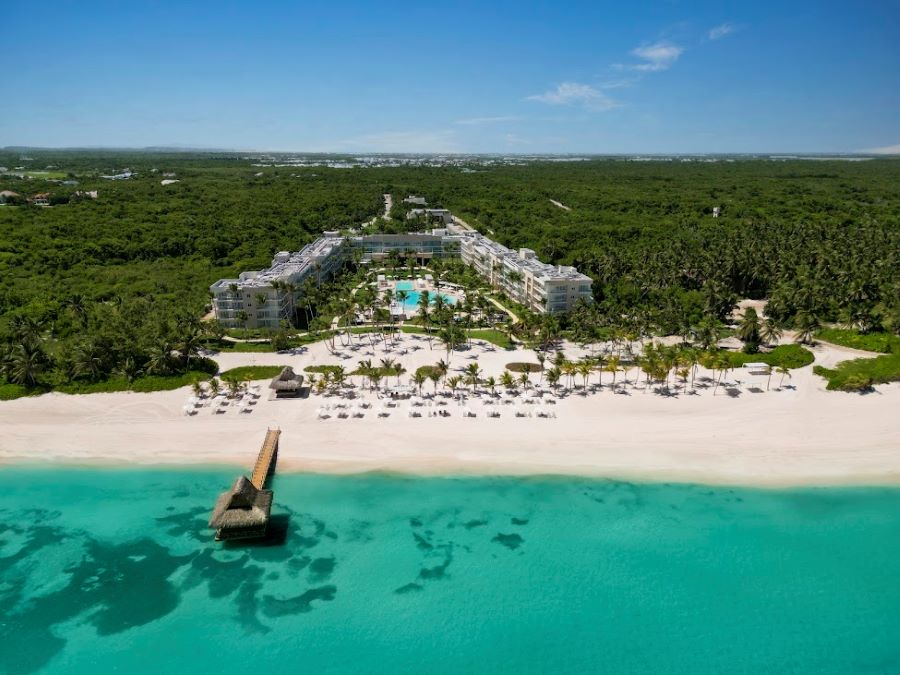 View of The Westin Puntacana Resort & Club with white sand beach and turquoise water in front of it and green trees behind