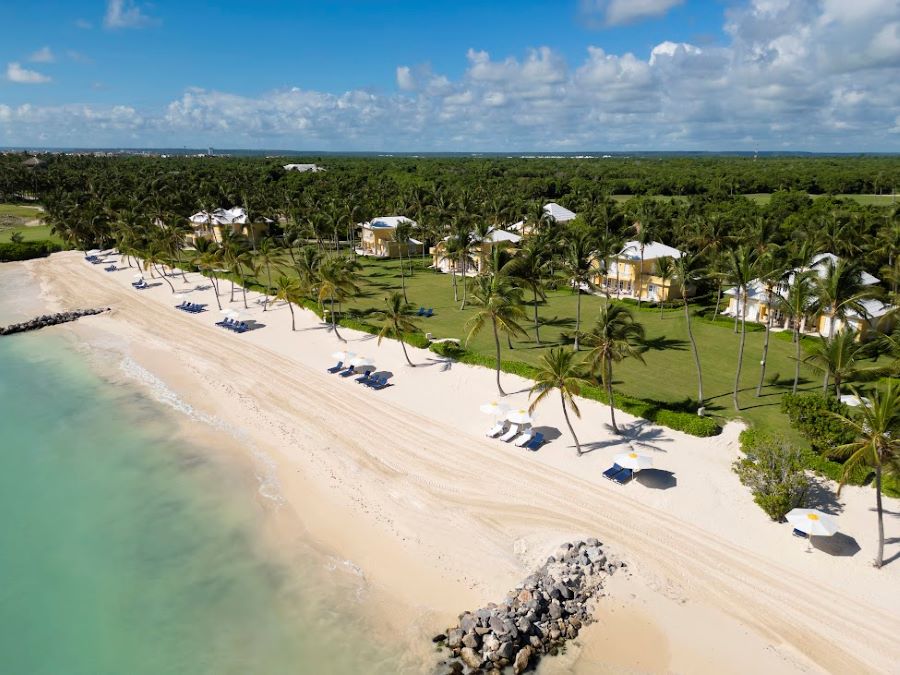 Beach view of Tortuga Bay Hotel at Puntacana Resort & Club with palm trees and sun loungers in front of the resort